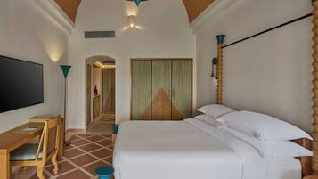 A hotel room with a bed, a desk, a chair, a TV, and a door leading to another room.