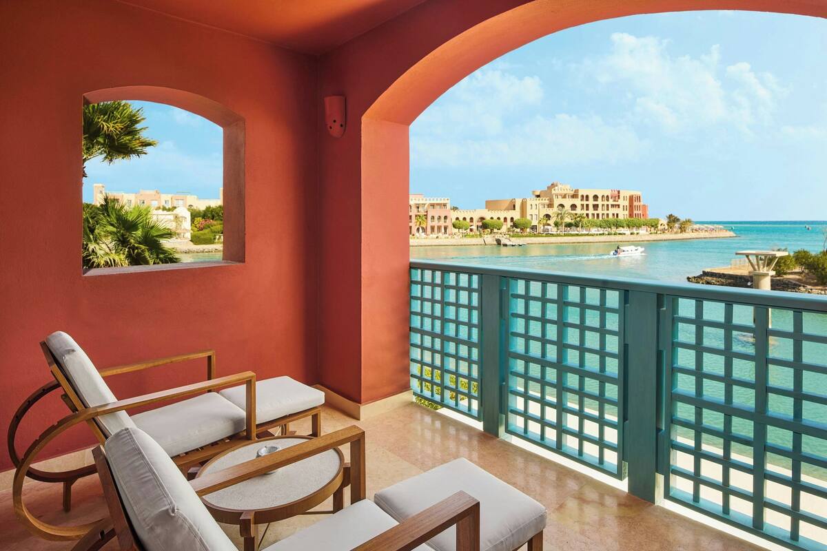 A balcony with two lounge chairs, a view of a coastal resort, and a clear sky.