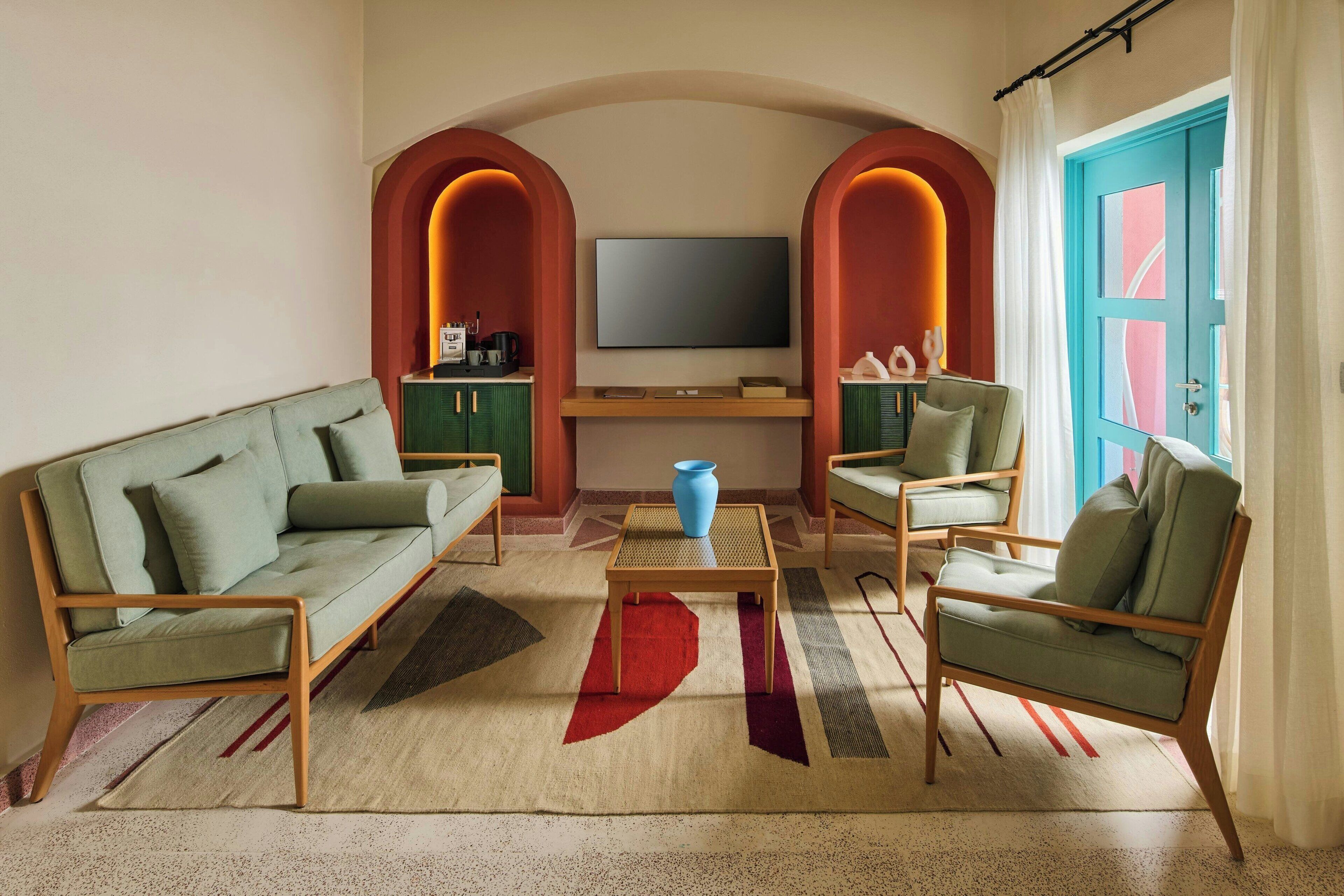 Un salón con sofá, sillones, una mesa de centro y un televisor montado en una pared con arcos.