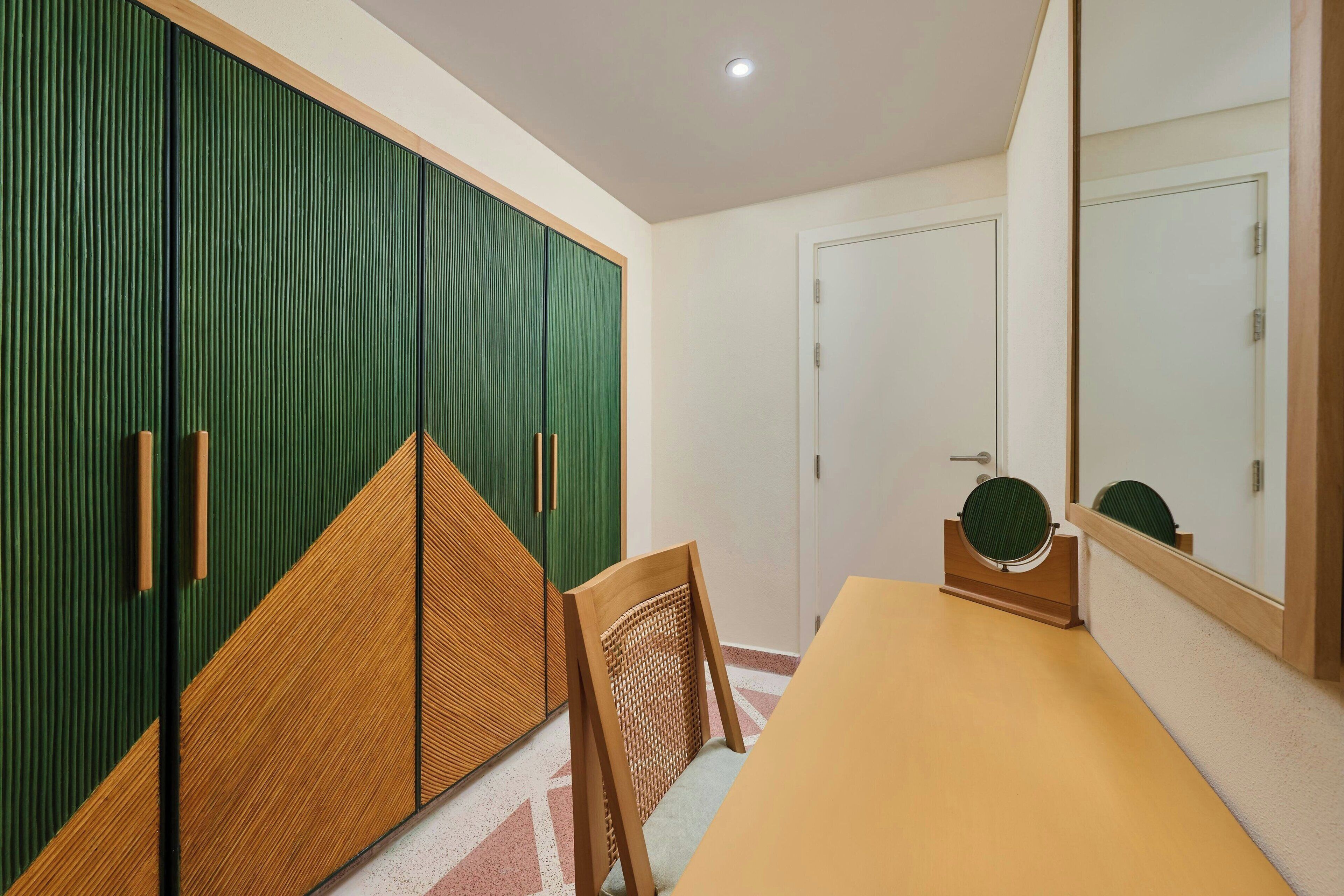 A room with a green wardrobe, a wooden chair, a table, and a mirror.