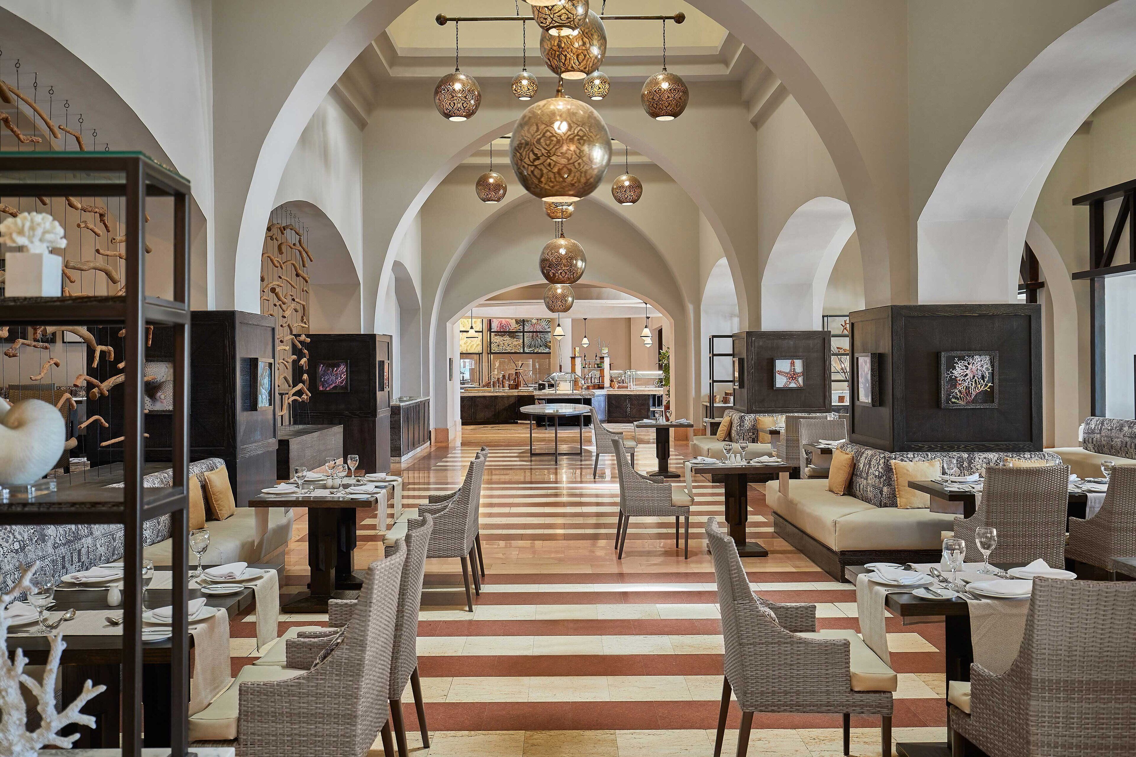 Un amplio vestíbulo de hotel con techos altos en arco, una zona central de comedor y diversas opciones de asiento, incluyendo sofás y sillones.