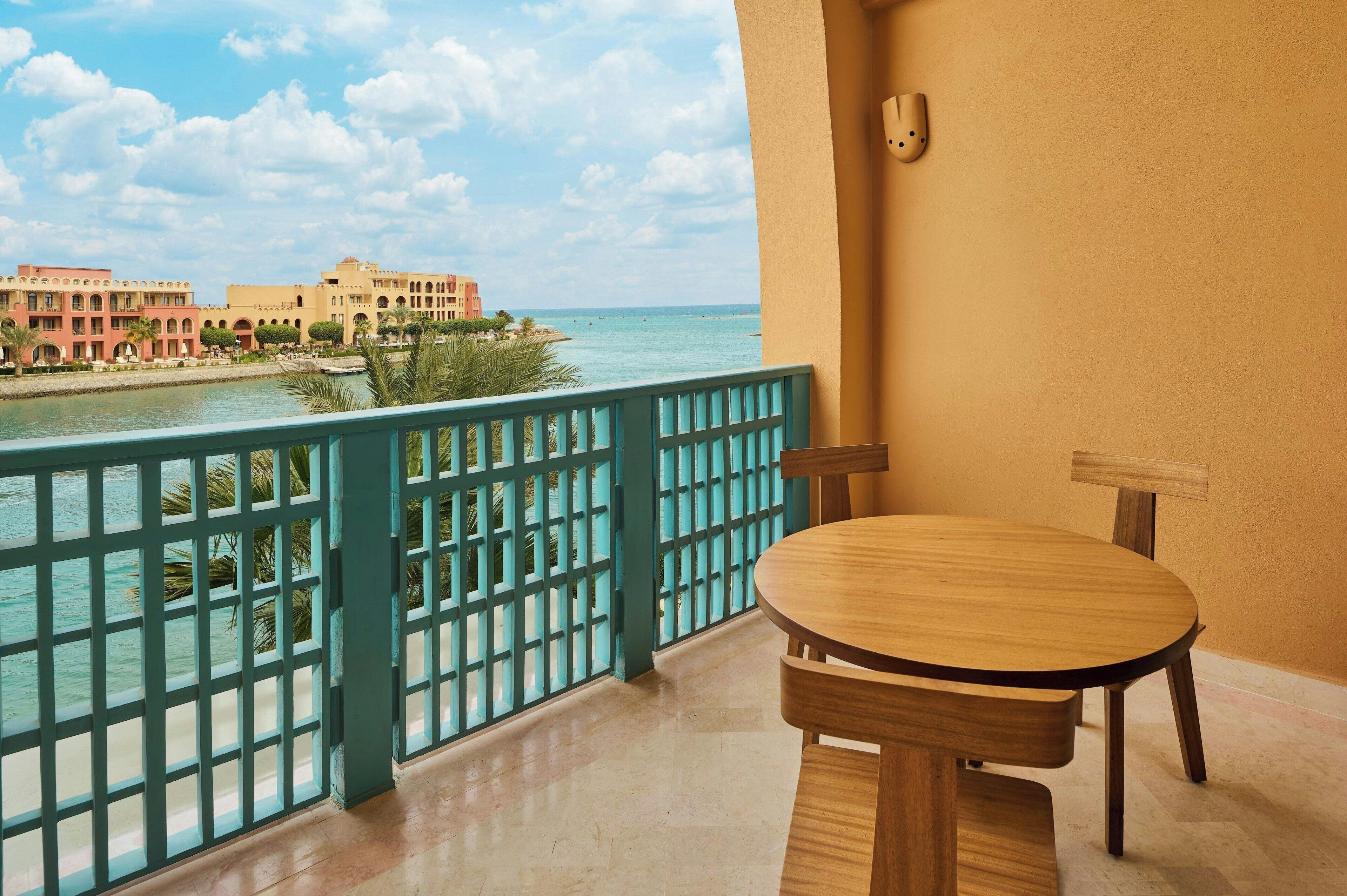 A balcony with a view of the sea, a wooden table, and a chair.