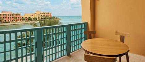 A balcony with a view of the sea, a wooden table, and a chair.