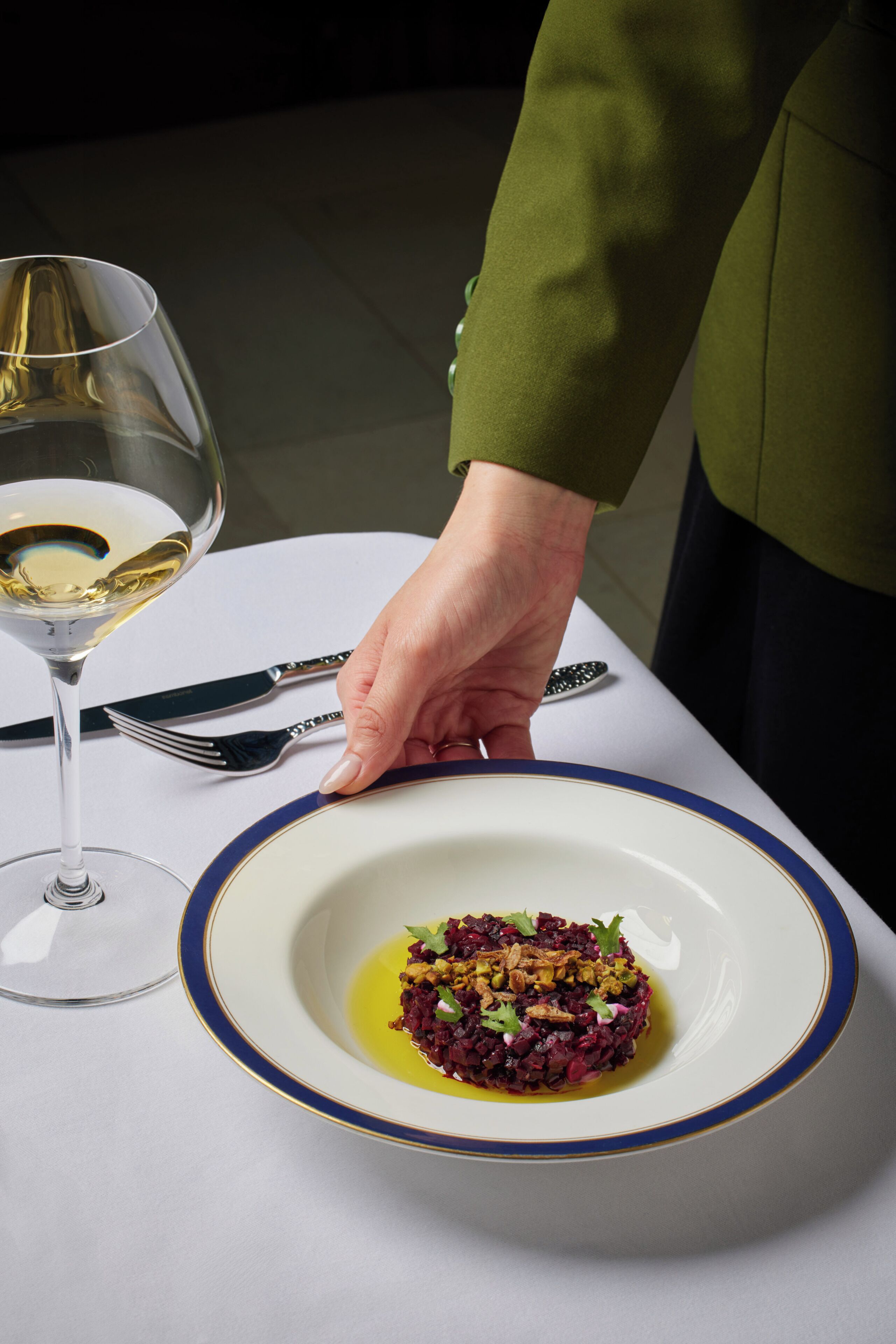 Un plato de comida sobre una mesa, con una copa de vino blanco y cubiertos.