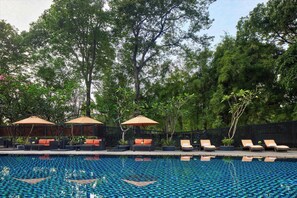 A swimming pool with lounge chairs and umbrellas, surrounded by trees. - Gran Melia Jakarta (Jakarta)