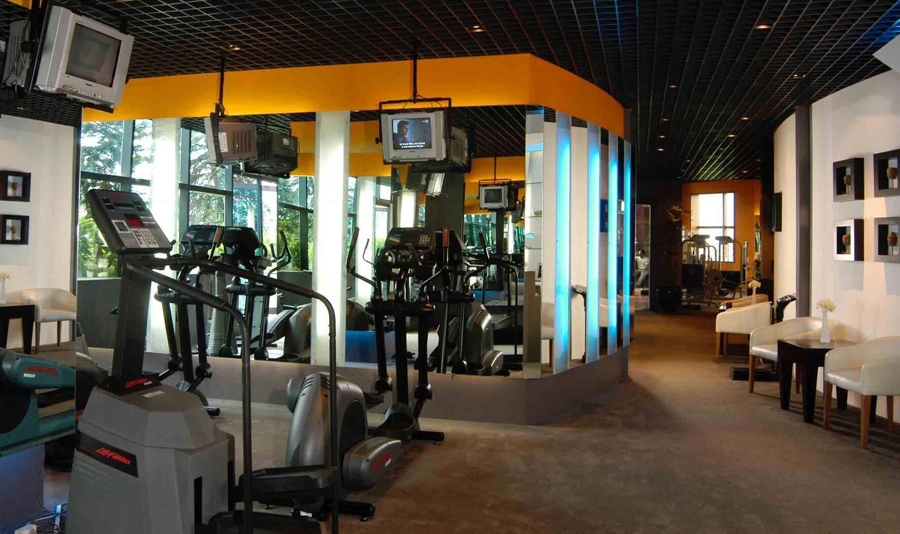 A gym with exercise equipment, a TV screen, and a seating area with tables and chairs.