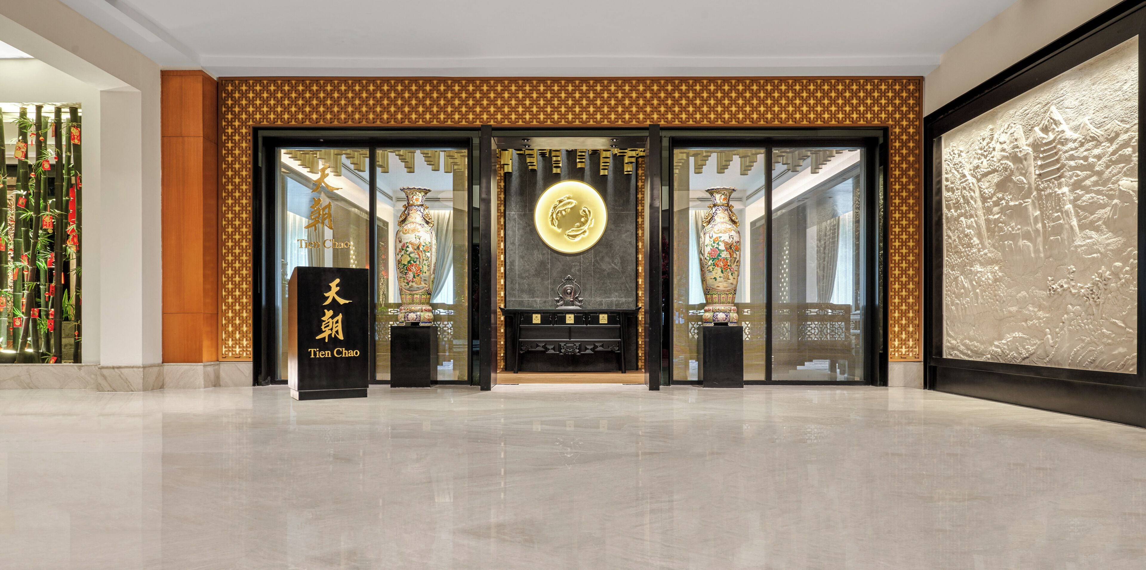 Entrada de un hotel con decoración china tradicional, que incluye un gran emblema dorado, dos jarrones ornamentados y un mostrador de recepción negro.