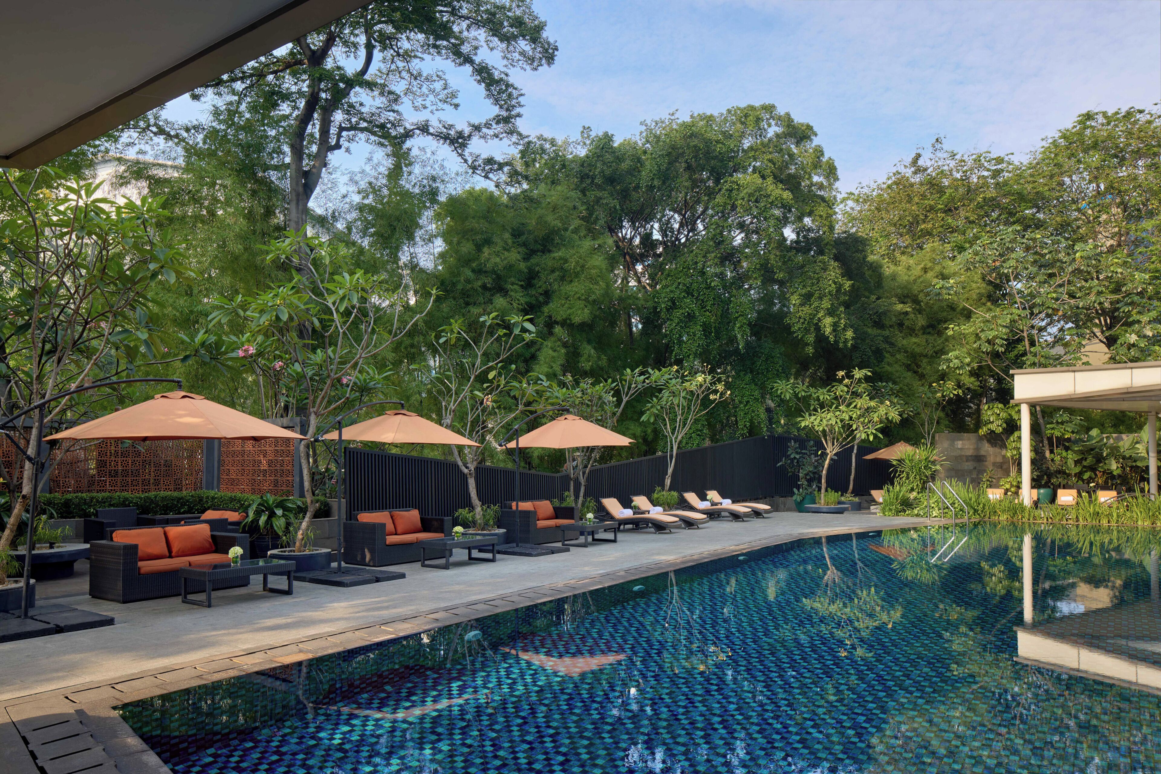 A swimming pool with lounge chairs and umbrellas, surrounded by greenery and trees.