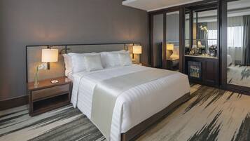 Habitación de hotel con una cama grande, dos mesitas de noche, un tocador, un espejo y piso alfombrado.