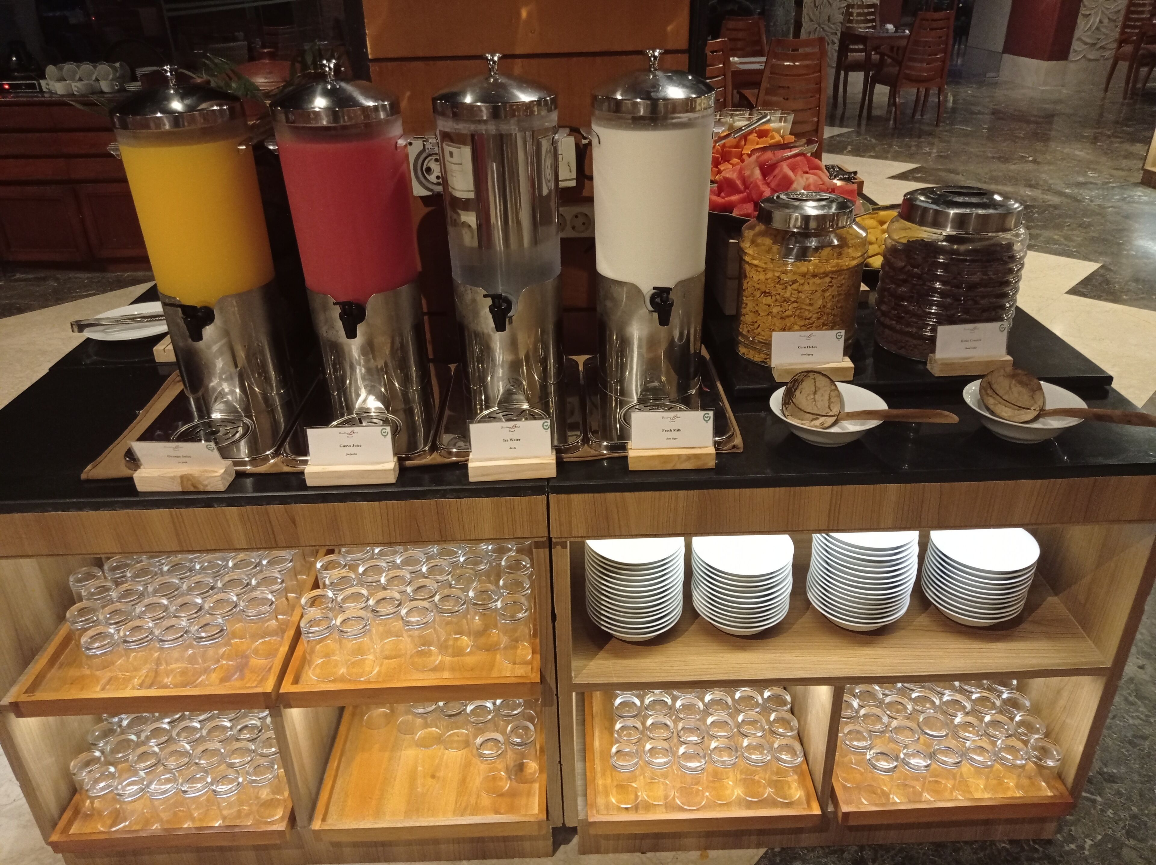 Disposición de buffet con varios dispensadores de bebidas, leche fresca, cereales y frutas.