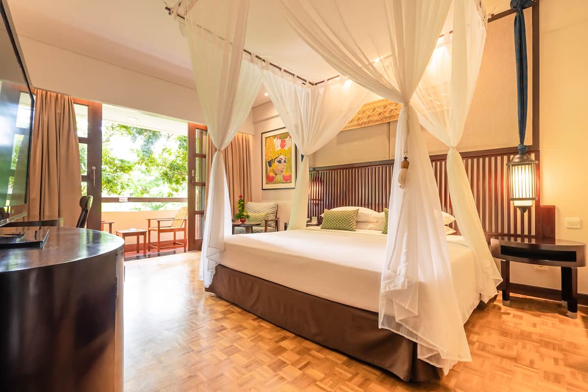 A bedroom with a four-poster bed, a bedside table, and a view of the outdoors.