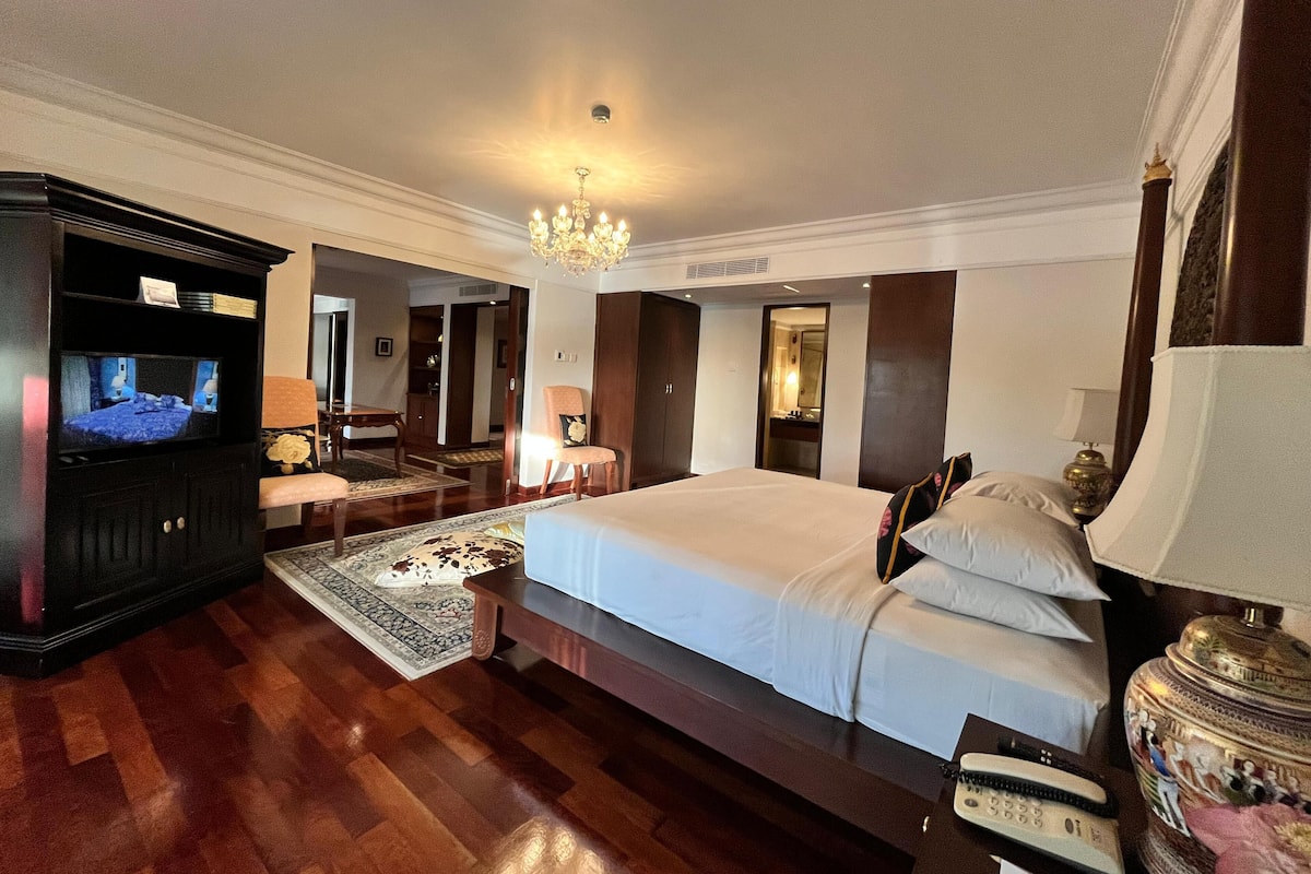 A hotel room with a large bed, a television, a desk, and a chandelier.