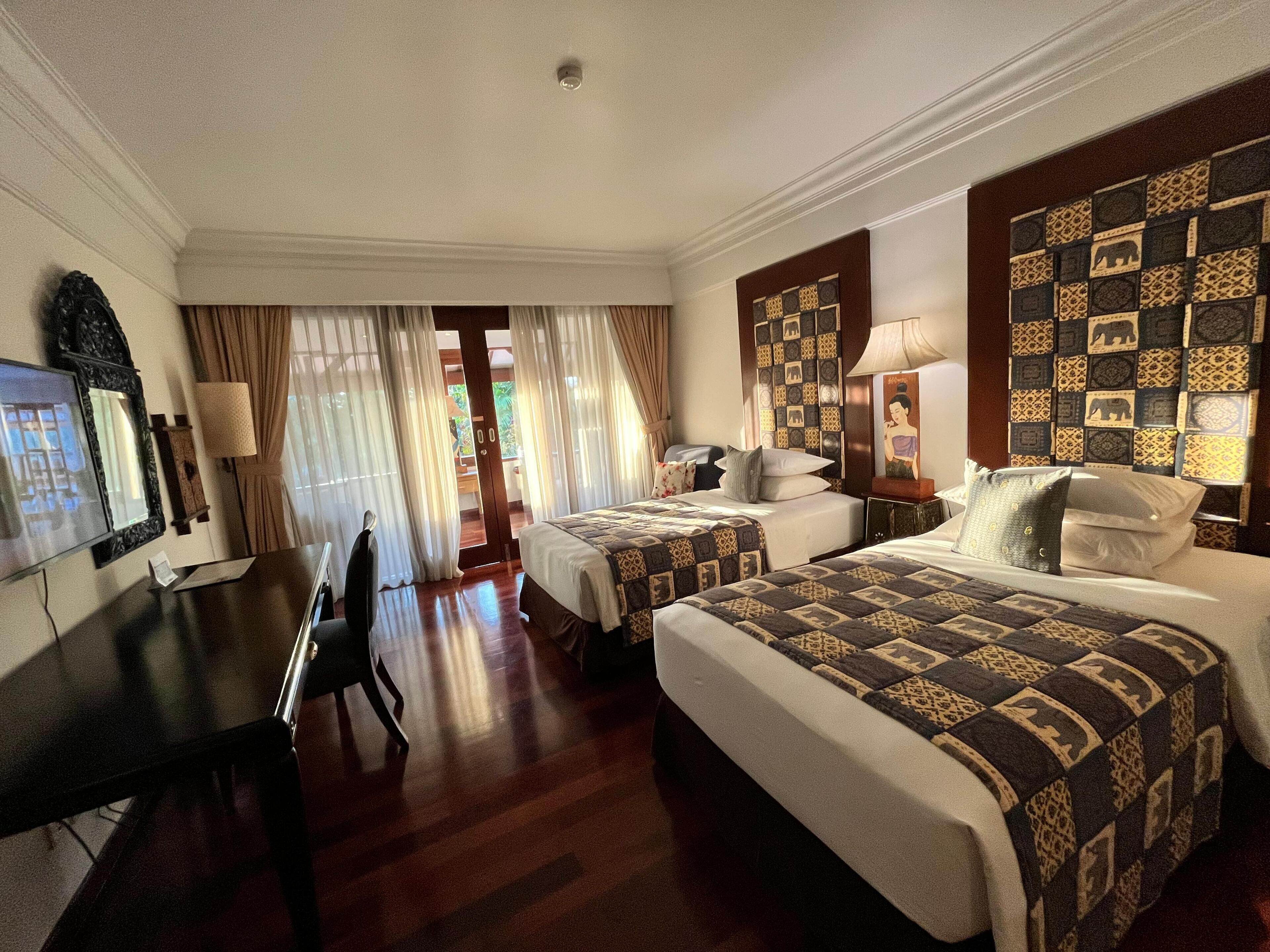 A hotel room with two beds, a desk, a chair, and a television.