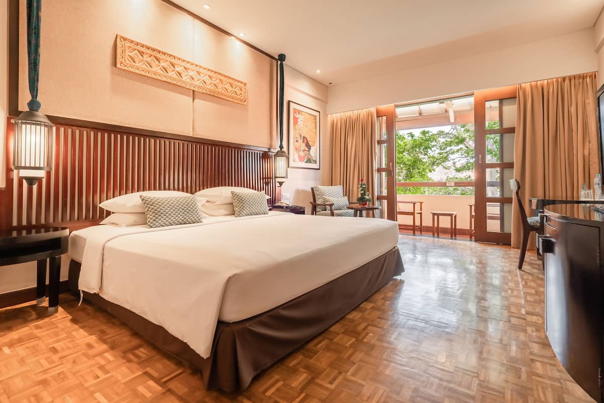 A hotel room with a large bed, wooden floor, a desk with a chair, and a view of the outdoors.