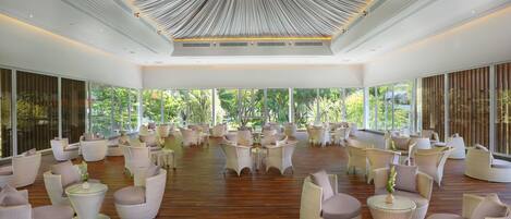 A spacious indoor area with multiple seating arrangements, large windows, and a unique ceiling design.