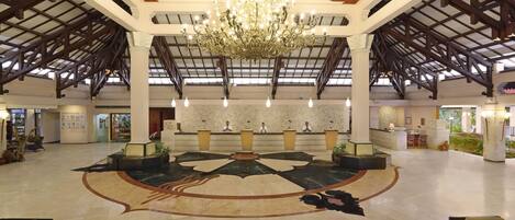 A spacious lobby with a high ceiling, a large chandelier, and a central seating area with a decorative floor design.