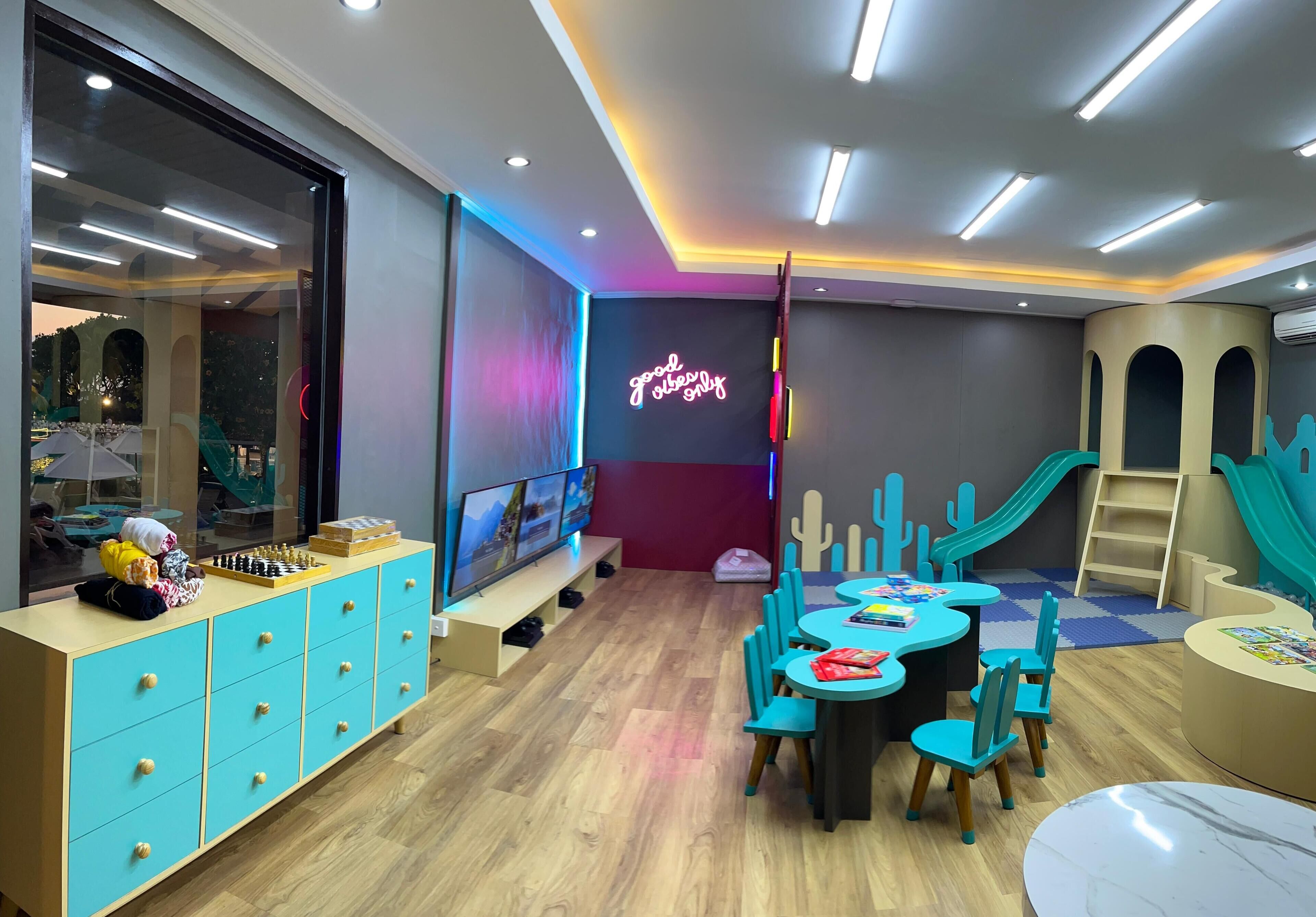 Una sala de juegos para niños con un letrero de neón, zona de recreación y una televisión grande.