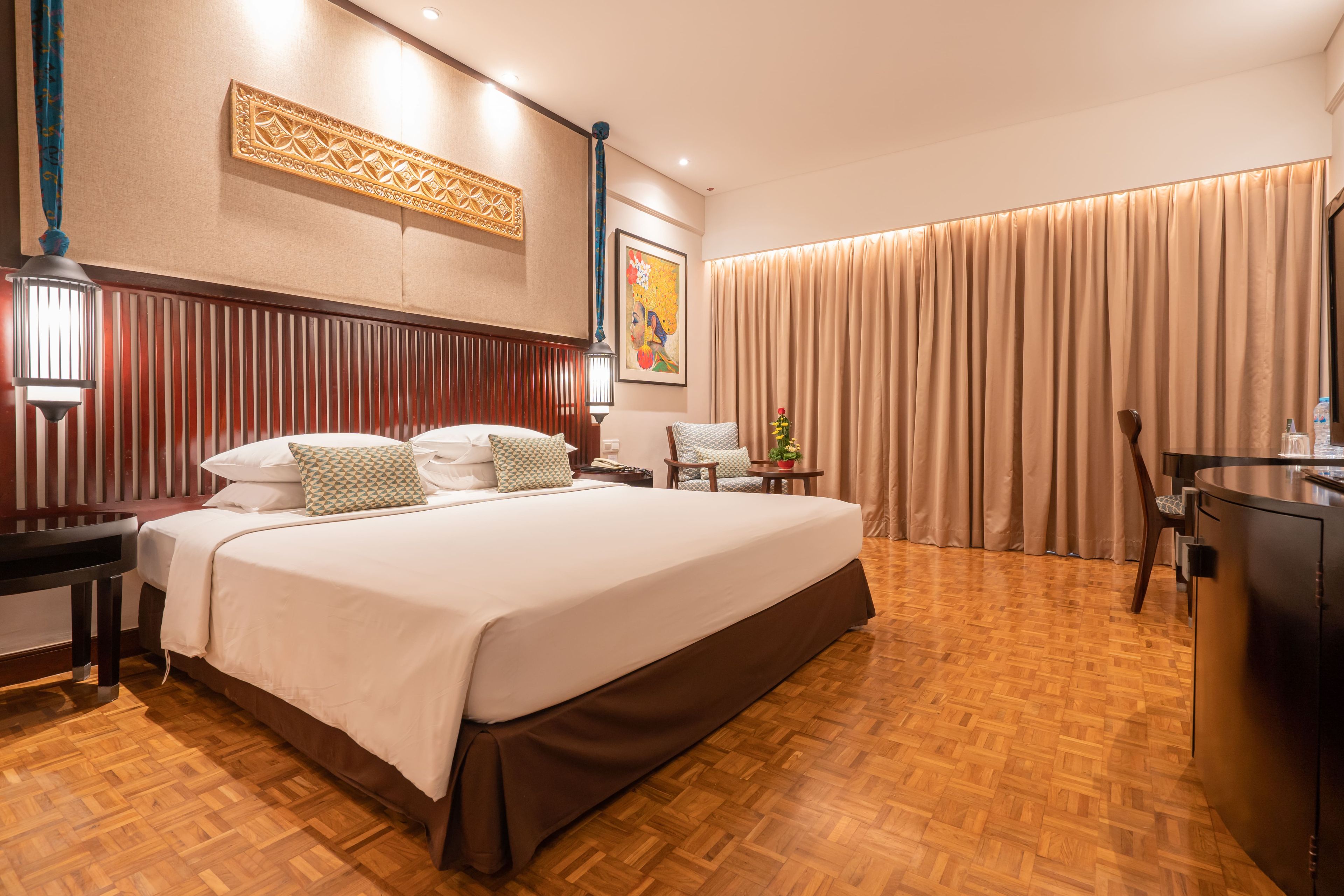 A hotel room with a large bed, a desk, a chair, a lamp, and a curtain.