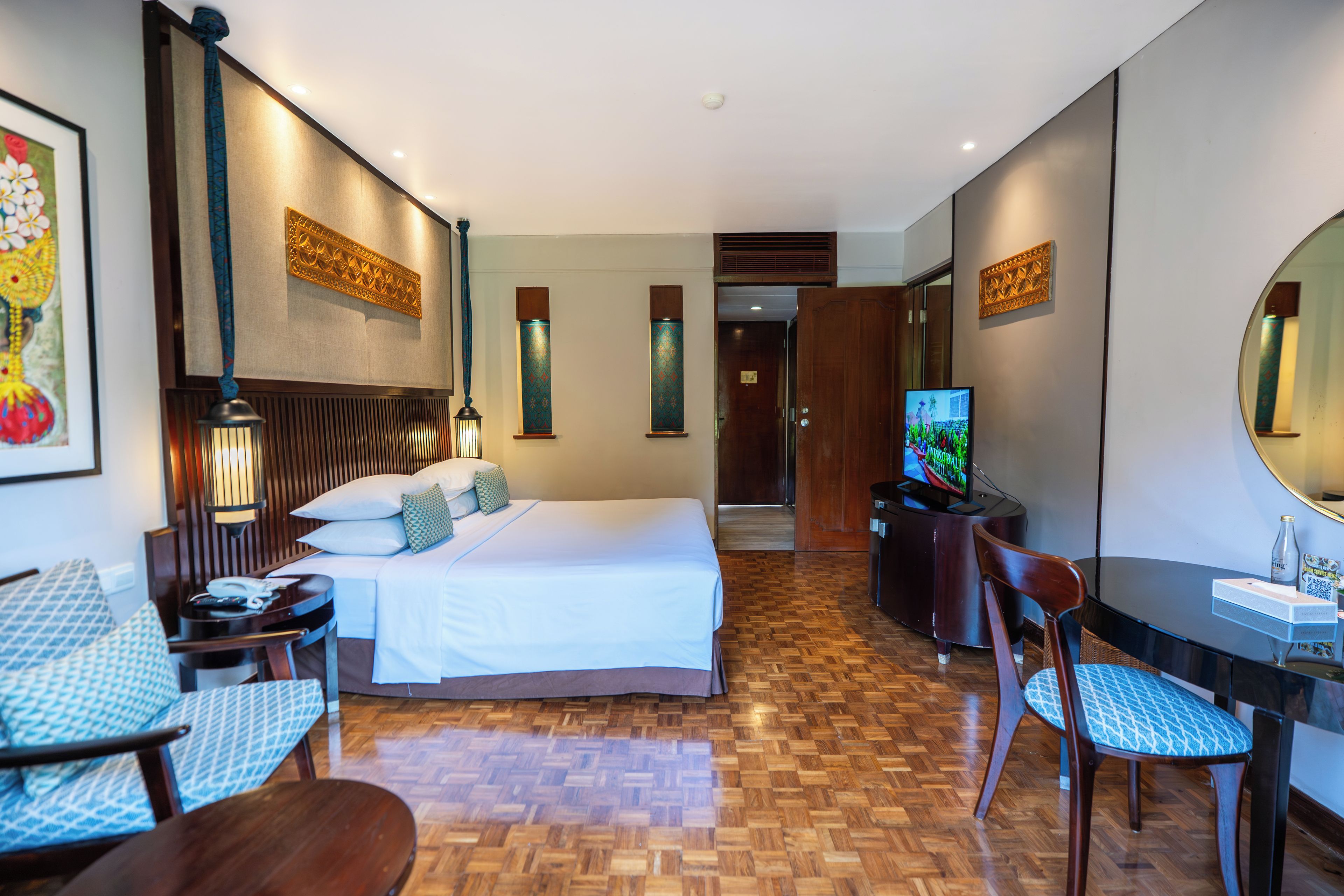 Habitación de hotel con cama, lámparas de noche, escritorio con silla, televisión y un espejo grande.