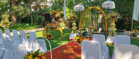 An outdoor wedding ceremony setup with white chairs, a floral carpet, and a decorative arch.