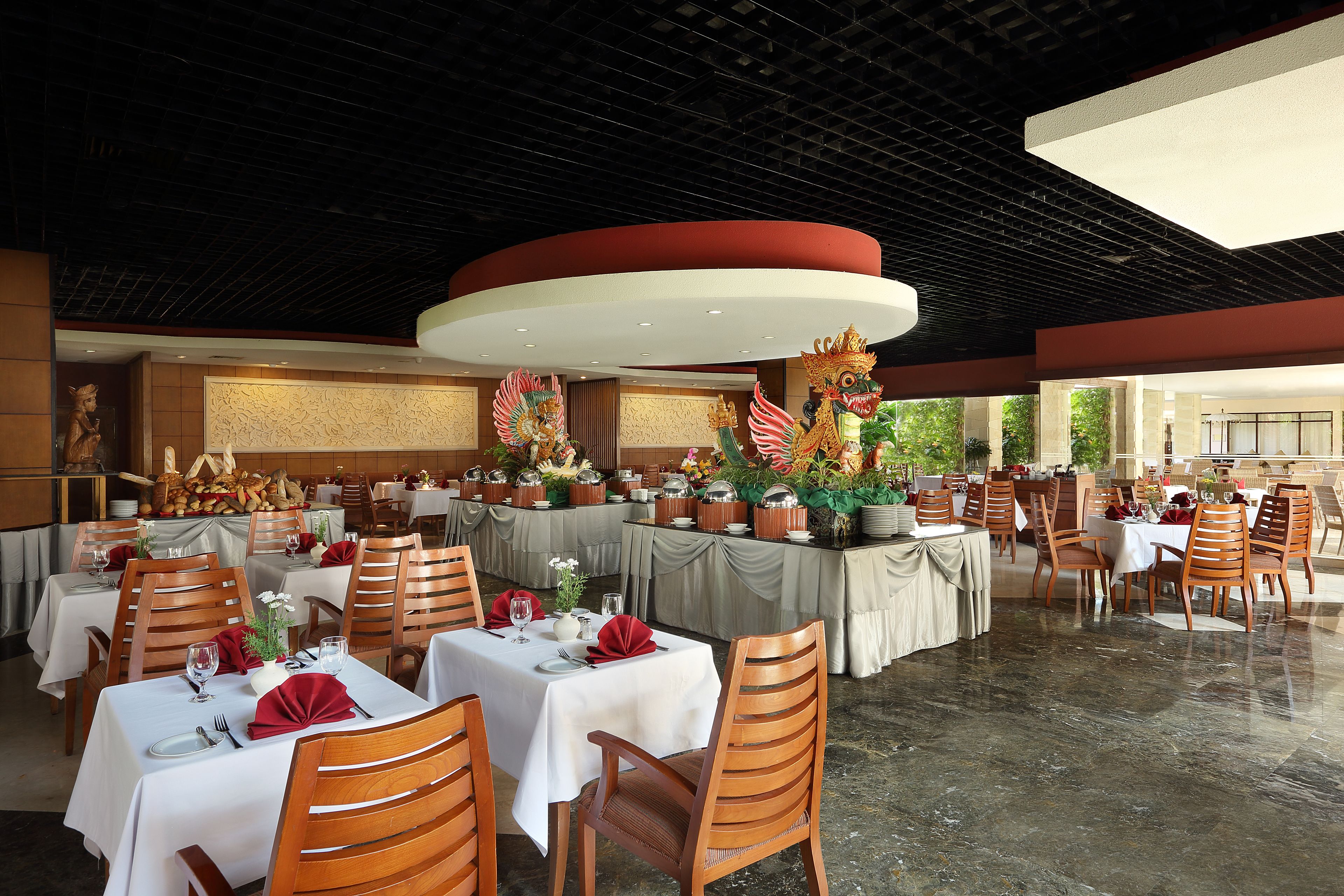 A restaurant with multiple tables, each set with white tablecloths, wooden chairs, and red napkins.