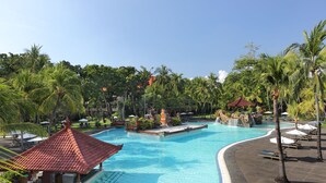 A large swimming pool with a tiled roof structure, surrounded by palm trees and lounge chairs.