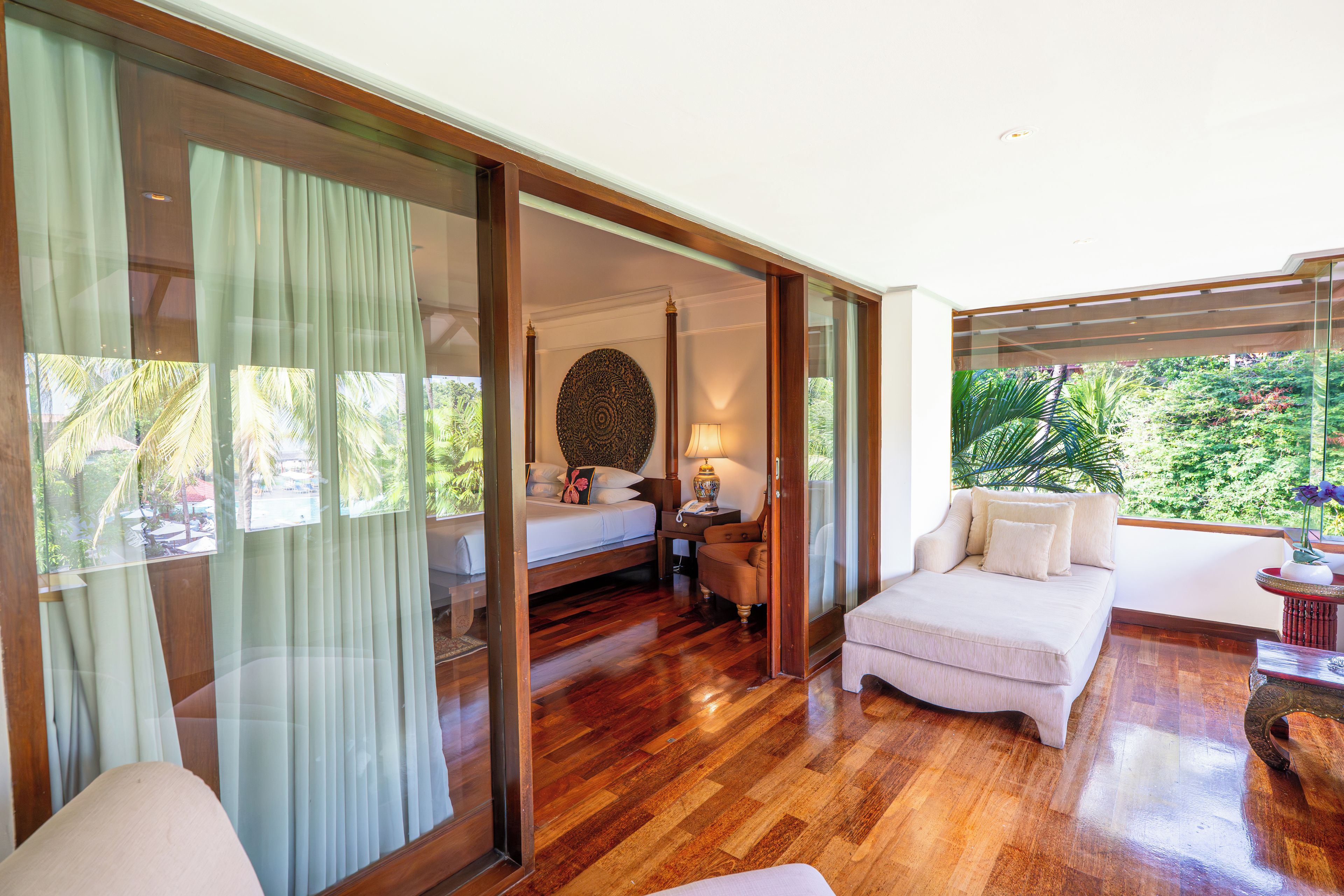 A room with a bed, a sofa, a desk, and a view of greenery.