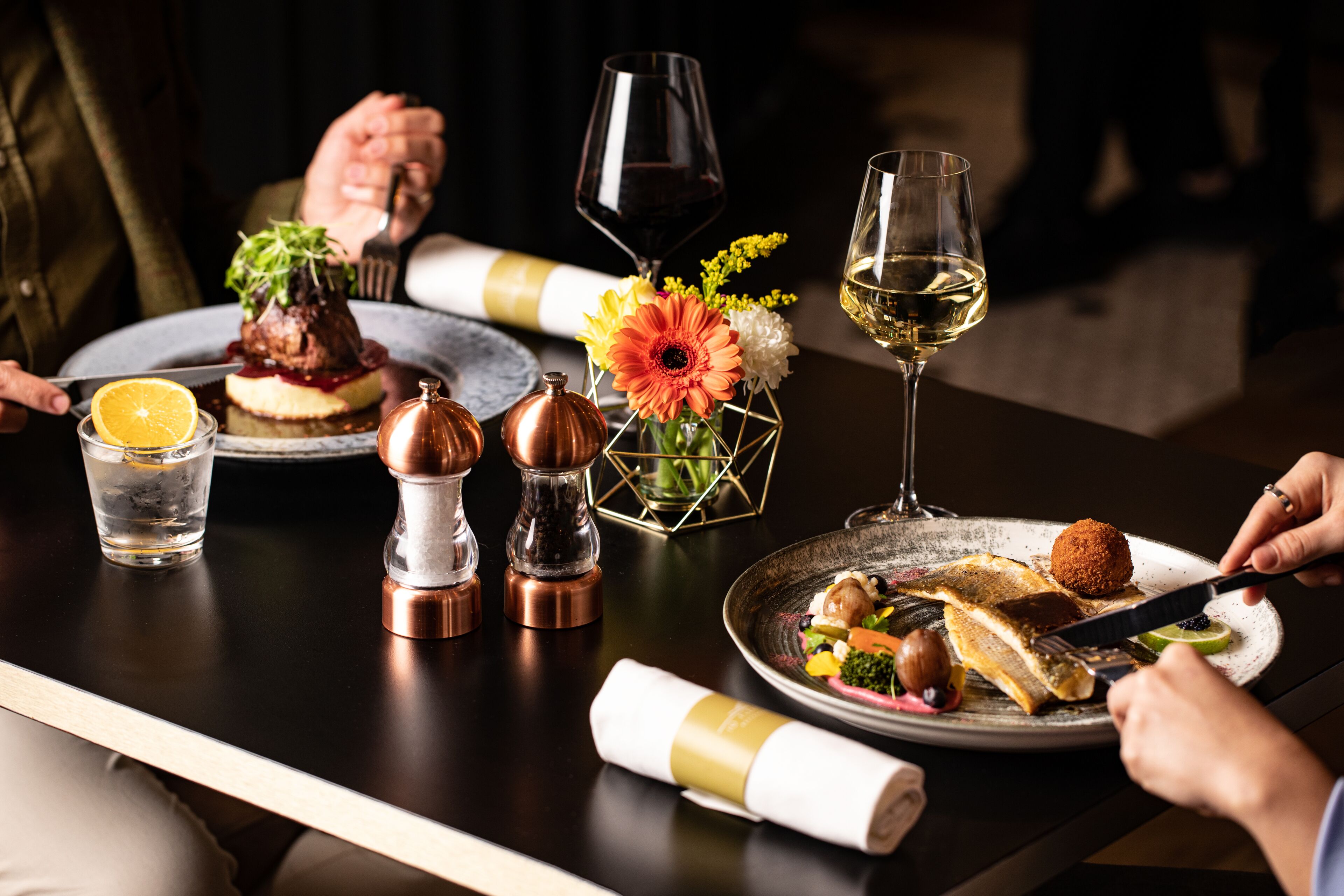Una mesa de comedor con platos de comida, copas de vino y un jarrón con flores.