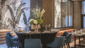Un comedor moderno con una mesa redonda dispuesta para seis personas, rodeada de sillas tapizadas en azul. Un ventanal ofrece vistas del exterior.