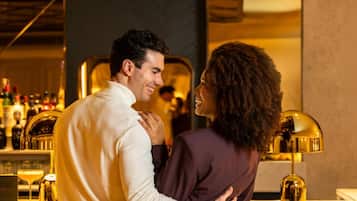 A couple embracing at a bar with a modern interior, including a bar counter and various bottles in the background.