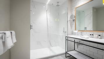 Un bagno moderno con doccia a parete in vetro, uno specchio grande e un mobile lavabo bianco con articoli da toilette.
