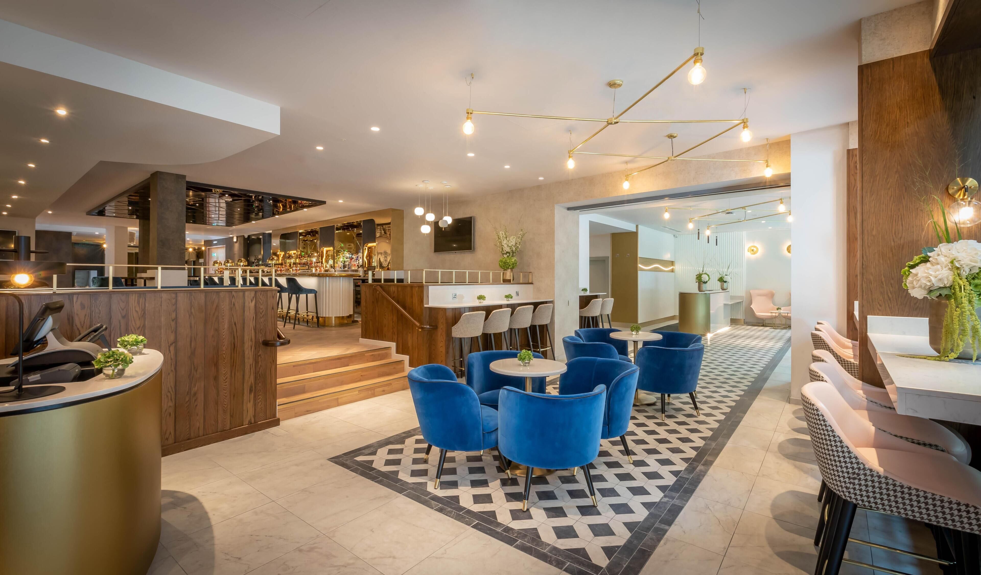 Un hall d’hôtel moderne doté d’un bar, de différents espaces de détente et d’un escalier menant à un étage supérieur.
