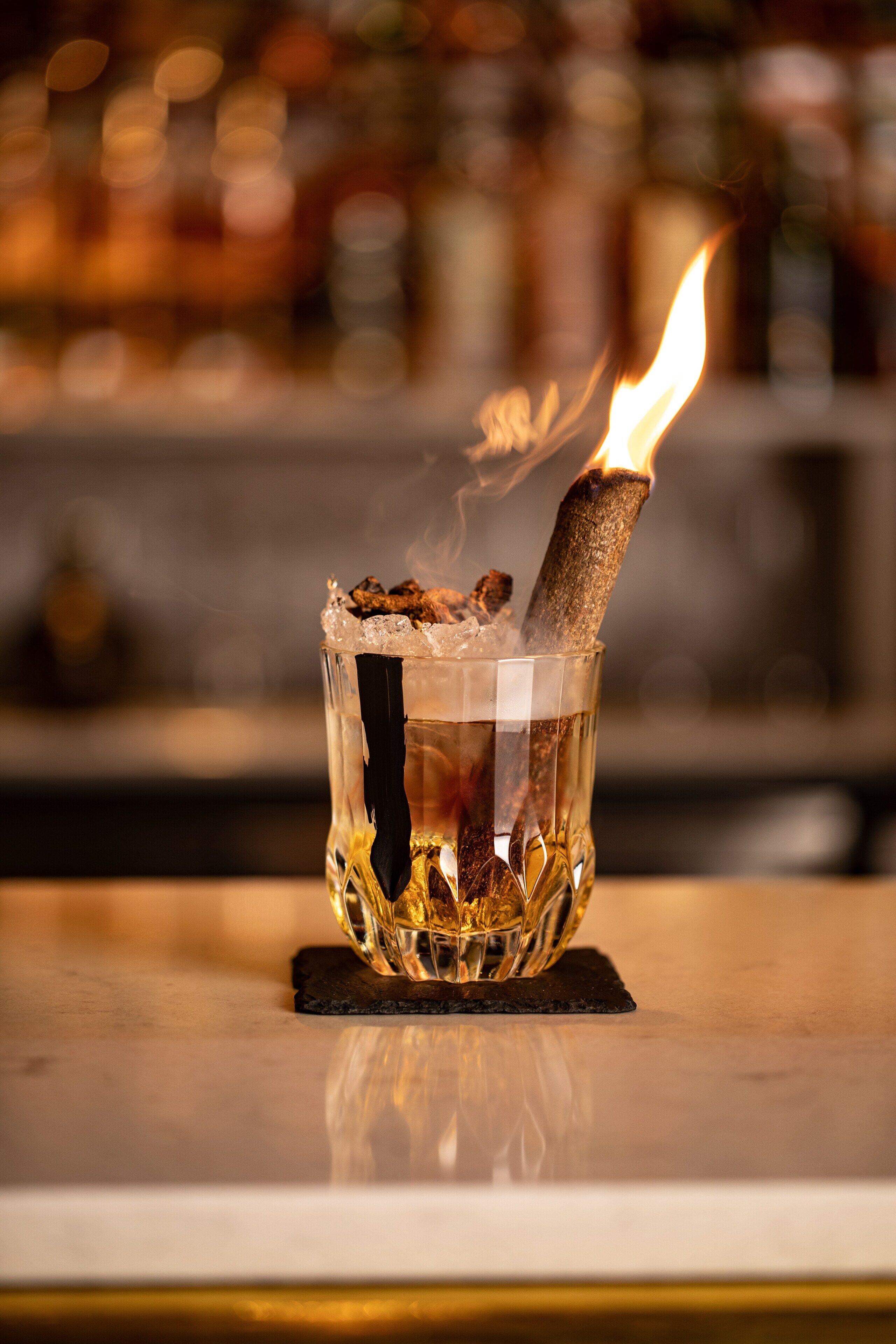 Un vaso con un palito encendido, sobre un posavasos.