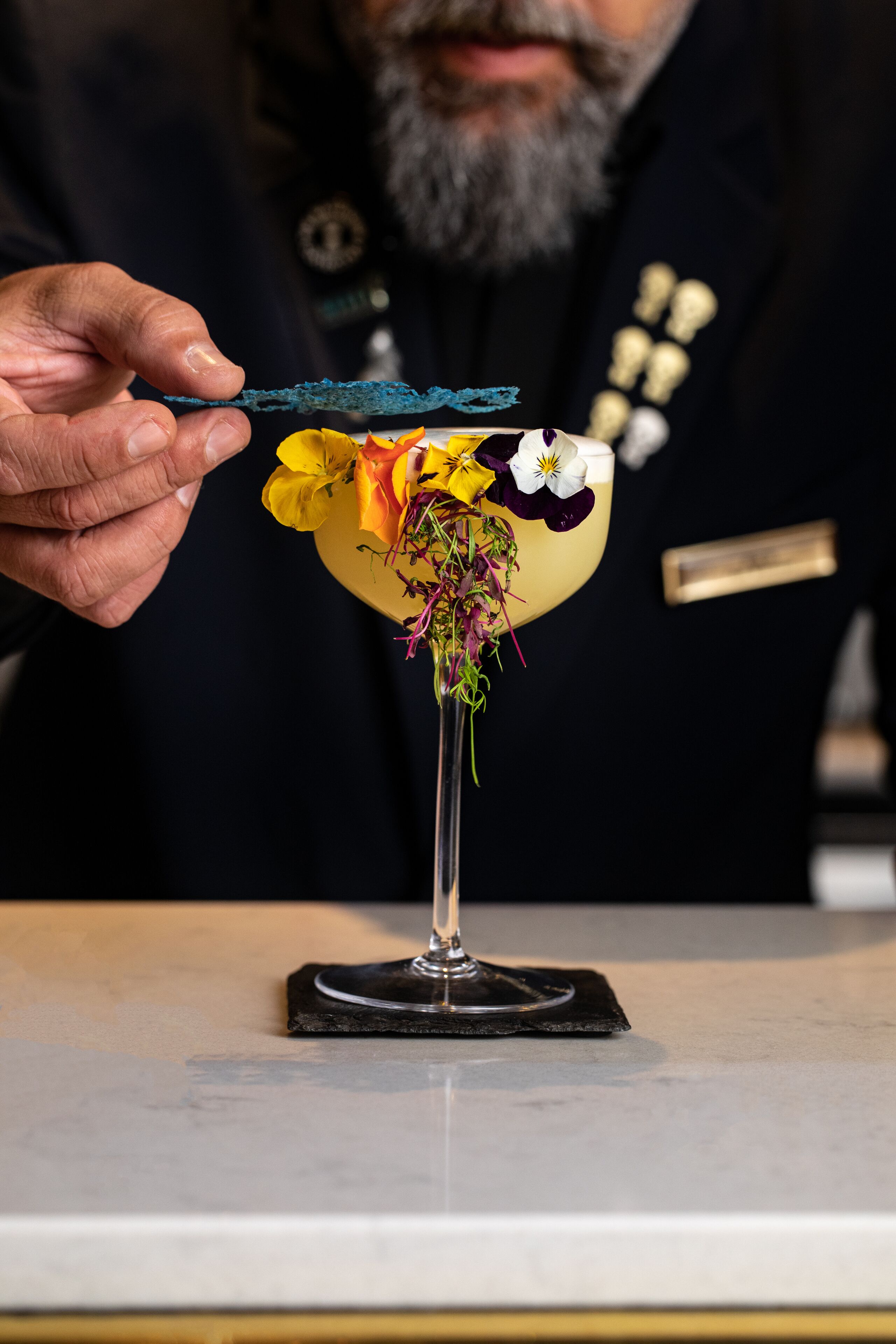 A person holding a cocktail with a colorful flower garnish.