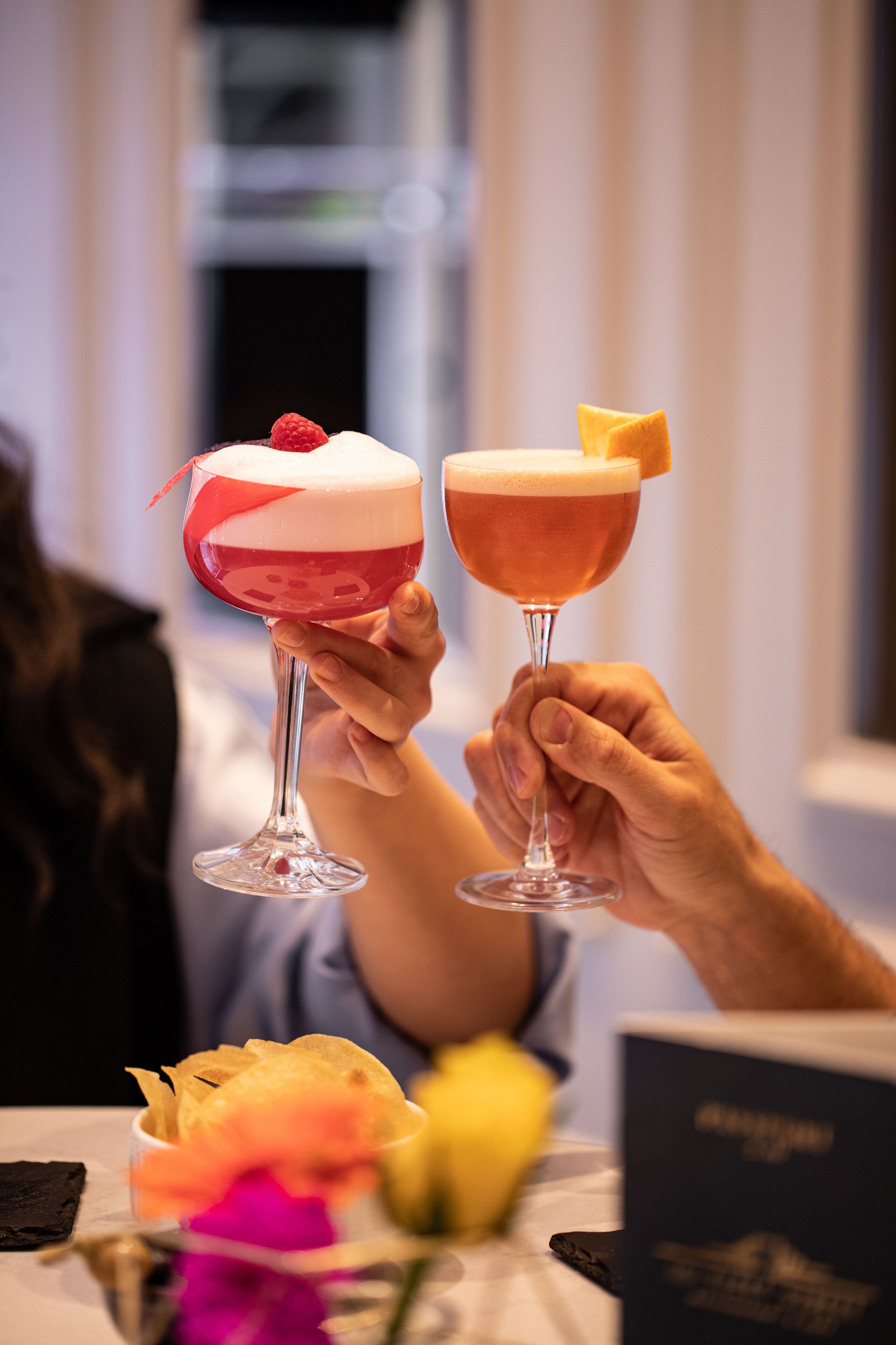 Two cocktails in stemmed glasses with a dessert on top, held by a person.