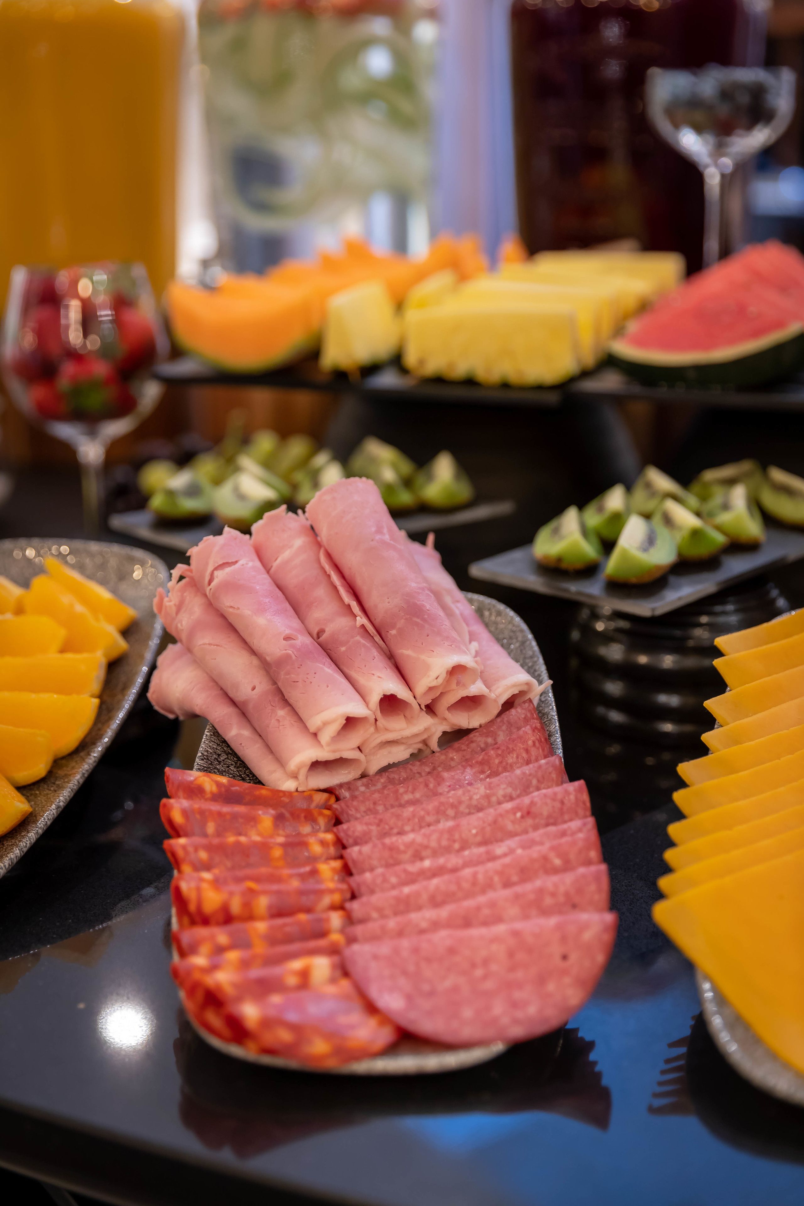 Una mesa de buffet con diversos alimentos, incluyendo carnes cortadas, quesos y frutas.