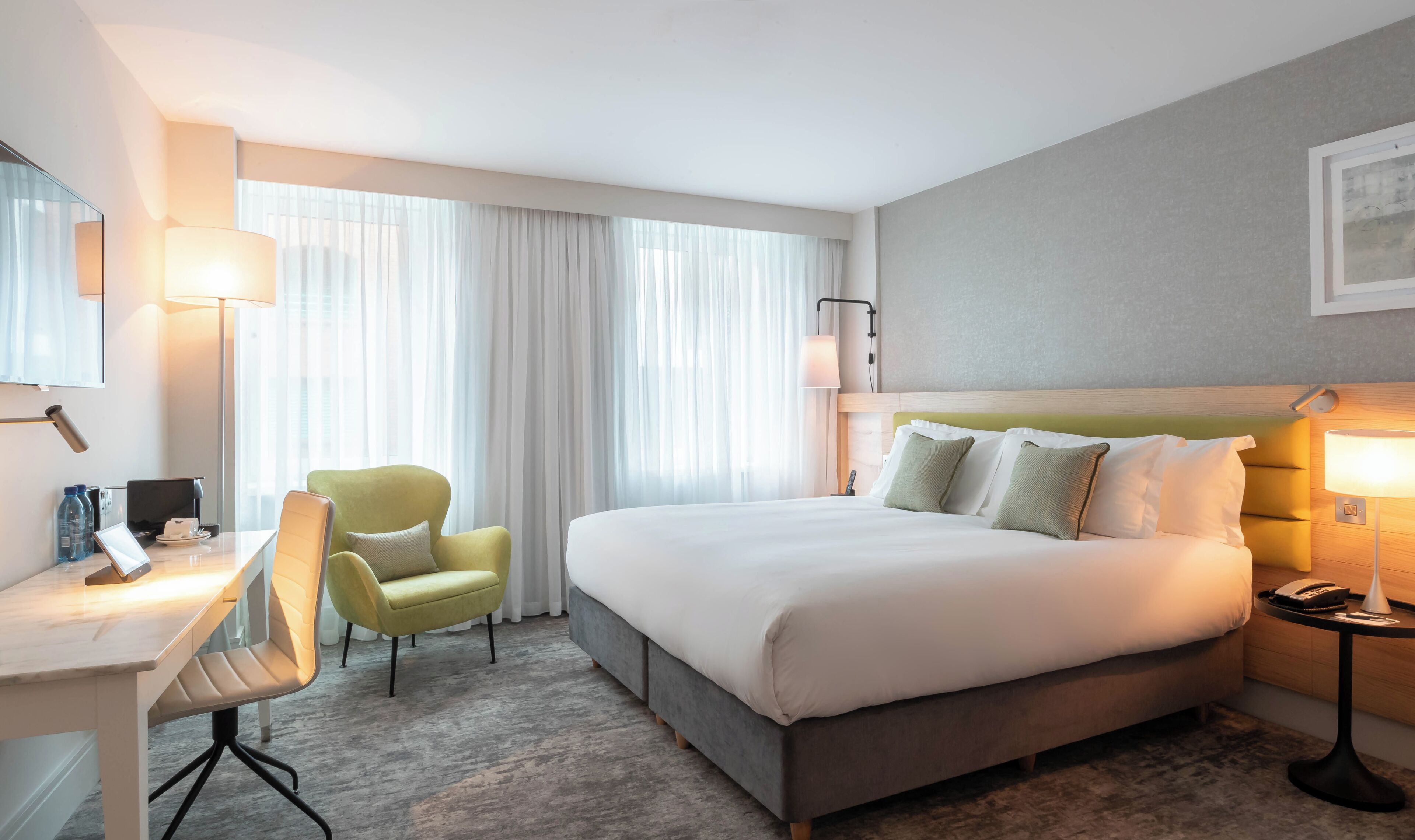 A hotel room with a bed, a desk, a chair, a lamp, and a telephone.