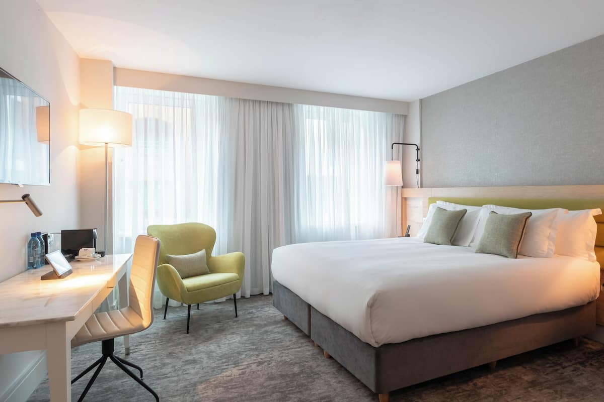 A hotel room with a bed, a desk, a chair, a lamp, and a telephone.