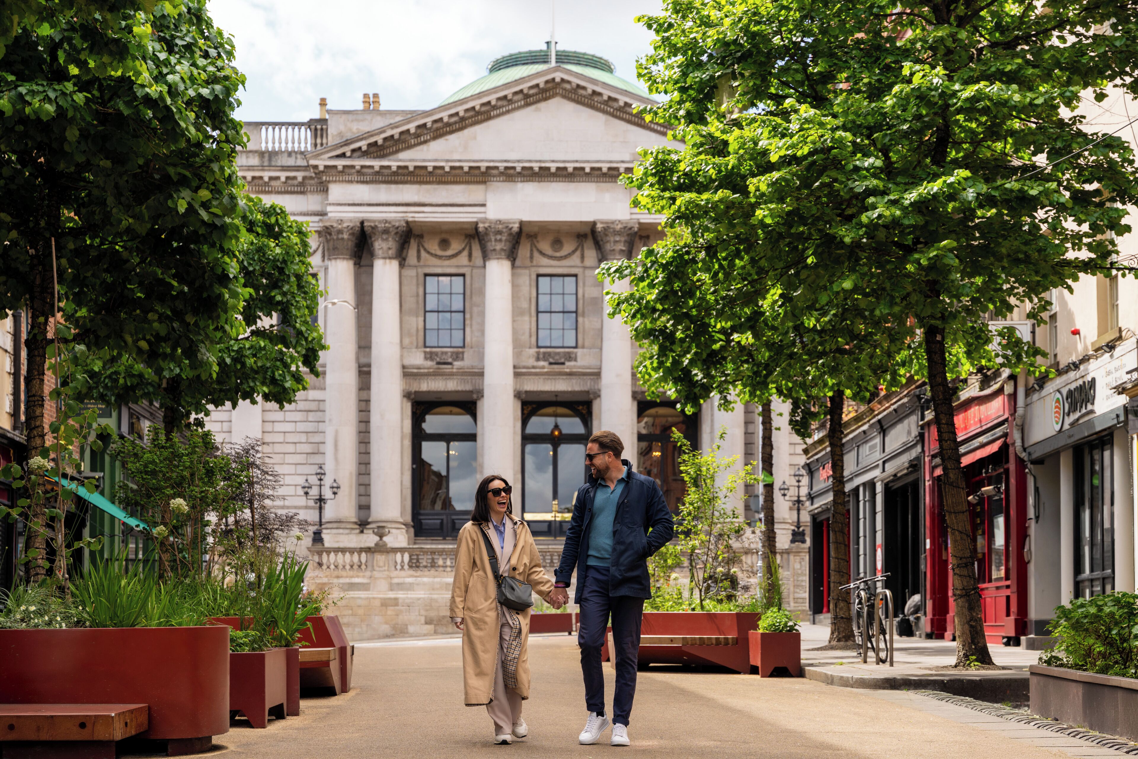 A couple walking on a pedestrian path with a classical building in the background.