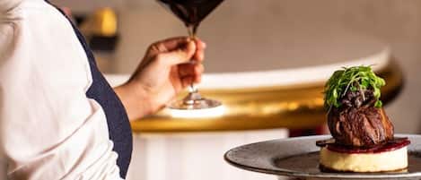 A person holding a plate with a dessert and a glass of red wine.