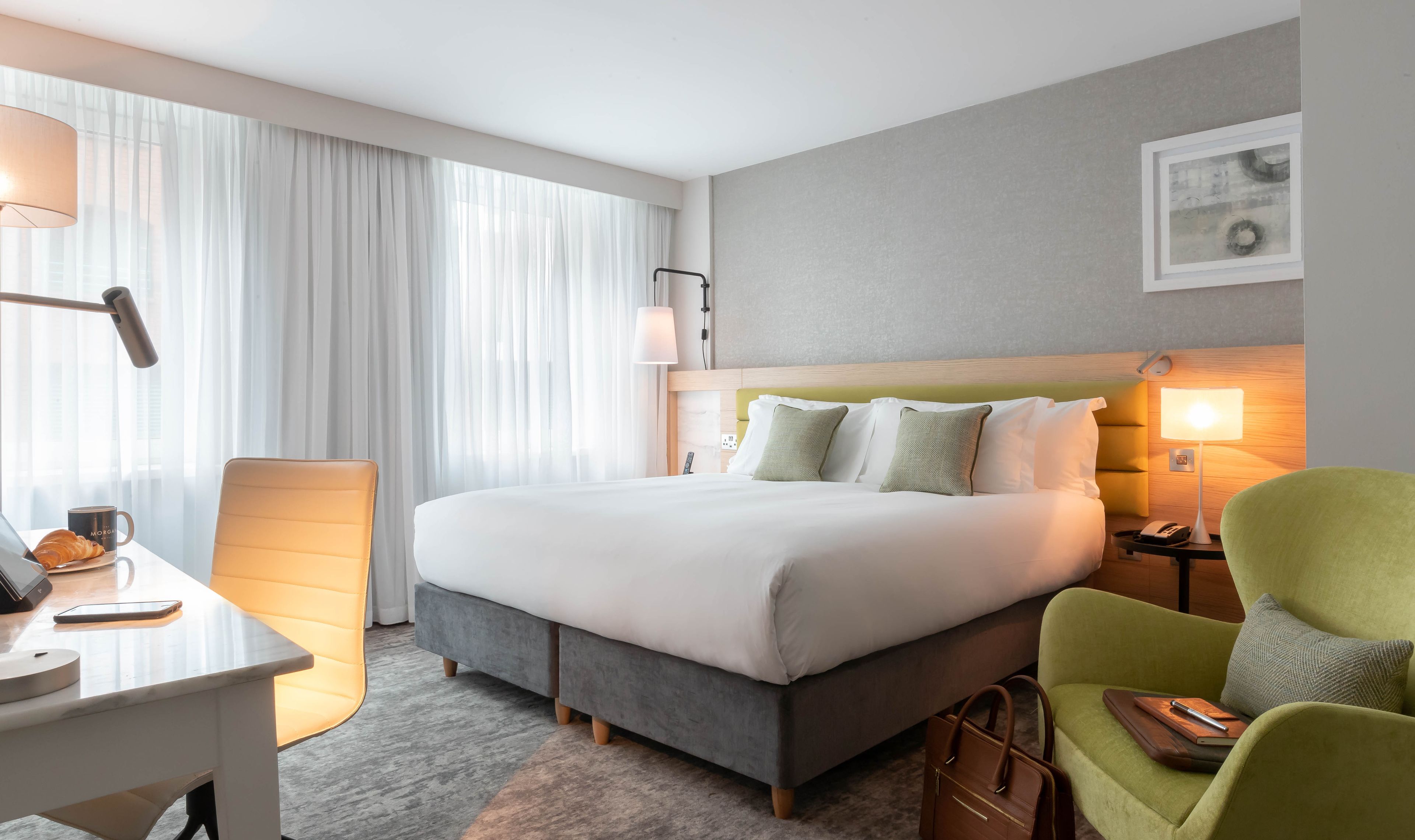 Habitación de hotel con una cama grande, un escritorio con lámpara, una silla y una mesita de noche con teléfono.