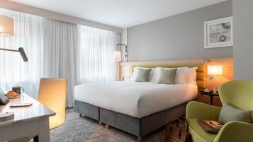 Habitación de hotel con una cama grande, un escritorio con lámpara, una silla y una mesita de noche con teléfono.