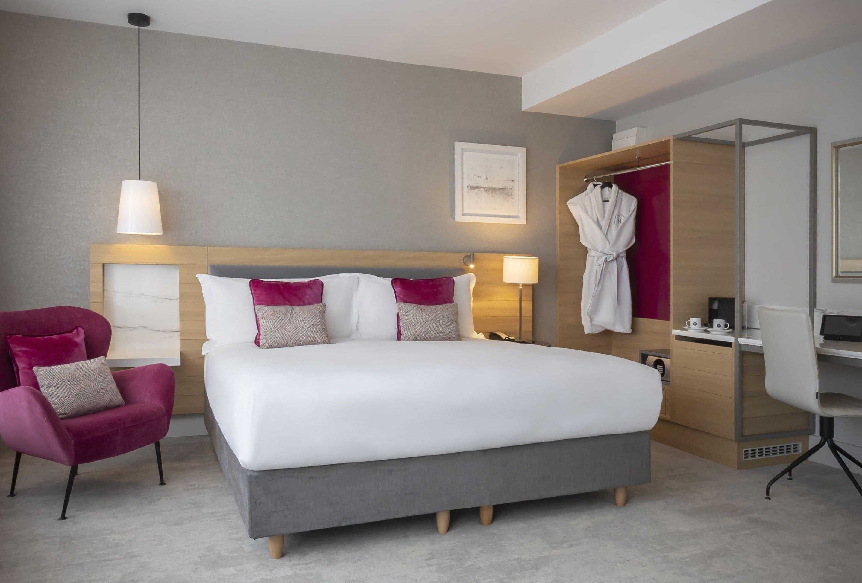 A modern hotel room with a large bed, a desk, a chair, and a robe rack.