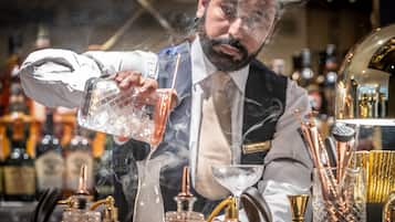 Un cantinero sirve una bebida en un vaso, rodeado de diversos utensilios y botellas de bar.
