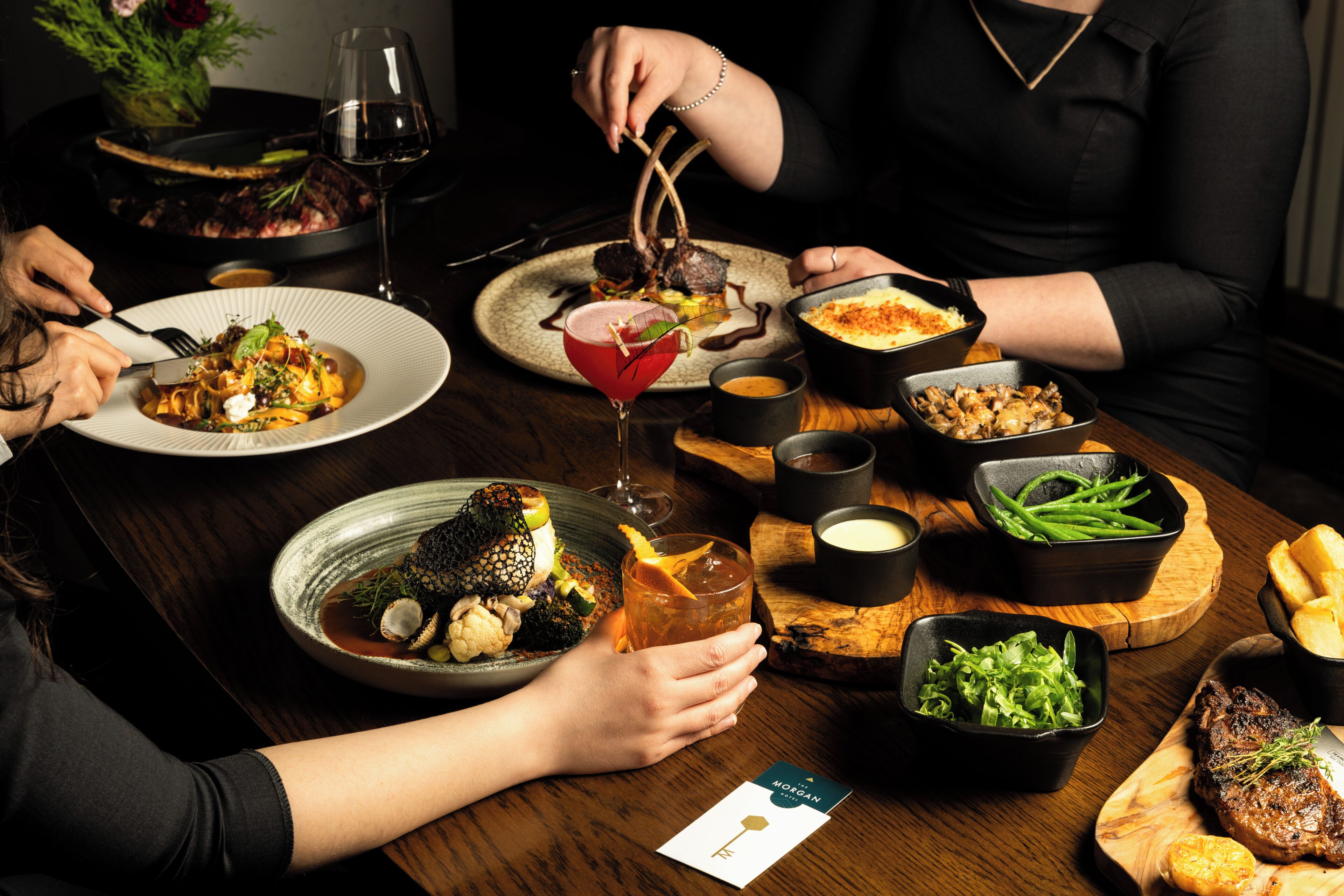 A dining table with various dishes, a glass of red wine, and a card on the table.