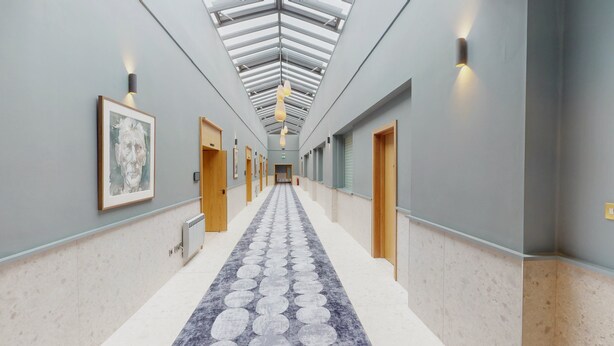 A hotel corridor with a skylight, framed artwork on the walls, and a patterned carpet.