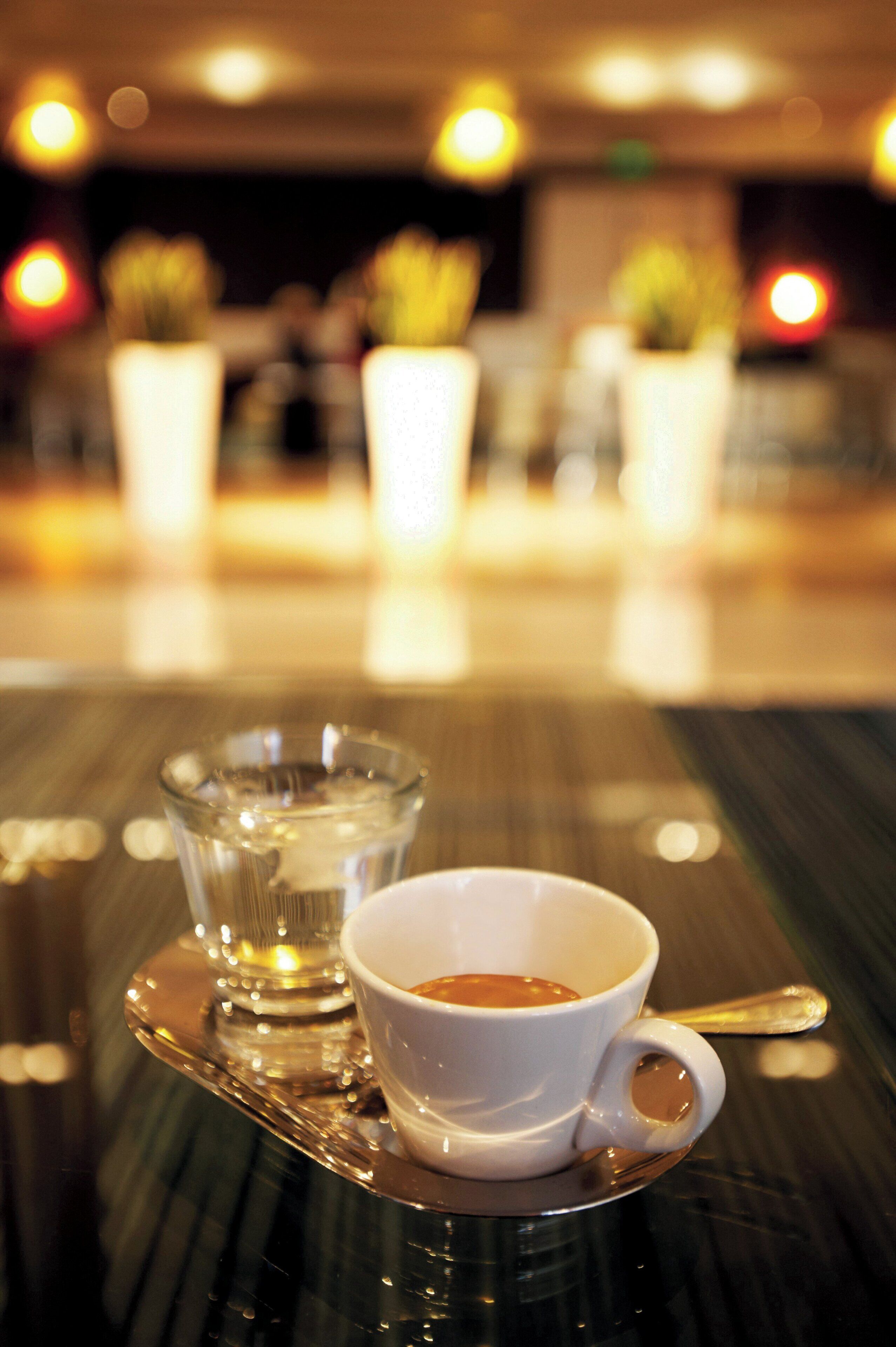 Ein Tisch mit einer Tasse Kaffee und einem Glas Wasser auf einer spiegelnden Ablagefläche.