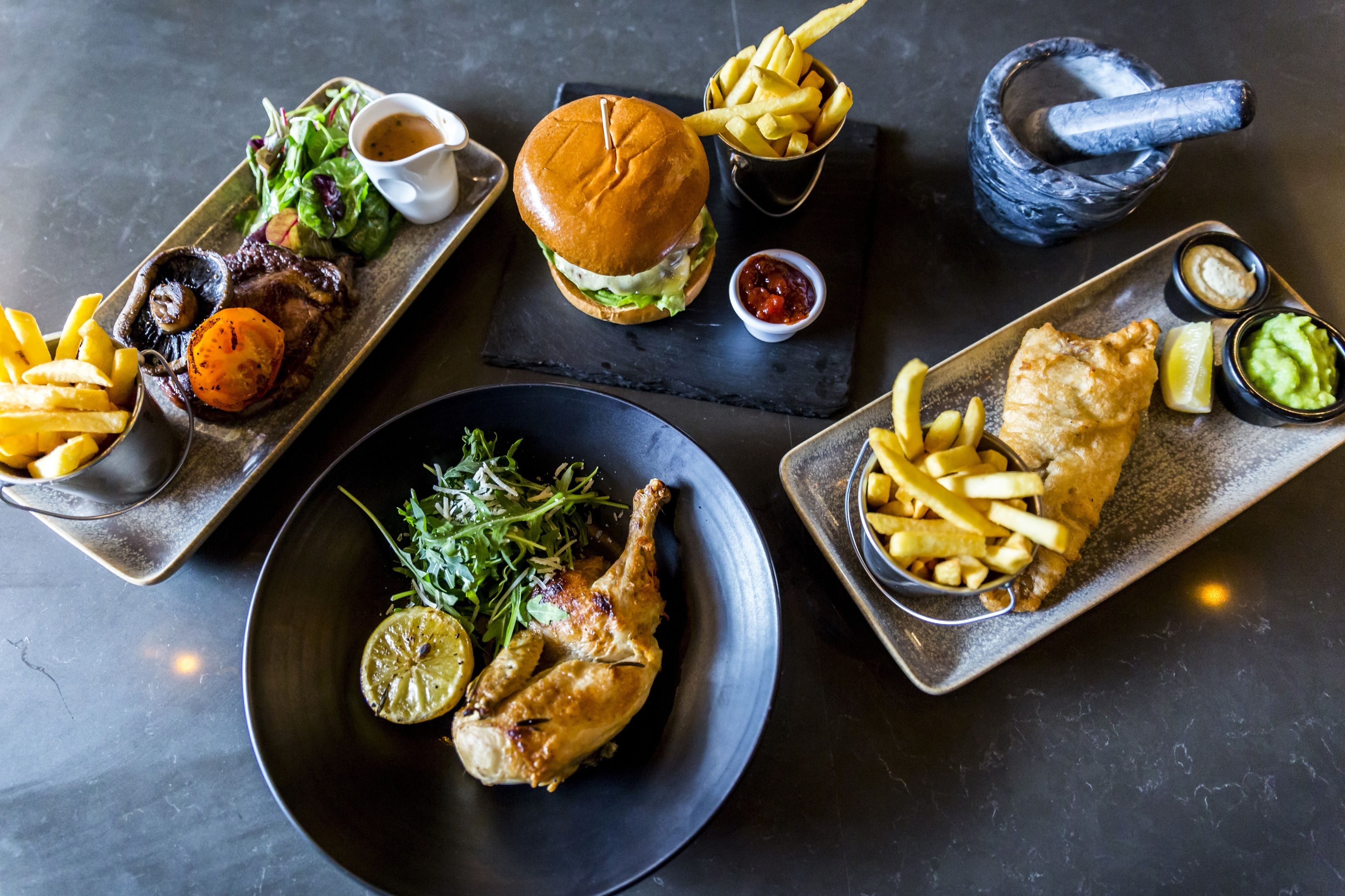 Diverse gerechten, waaronder een hamburger, fish and chips en een gebraden kip, gepresenteerd op verschillende borden.
