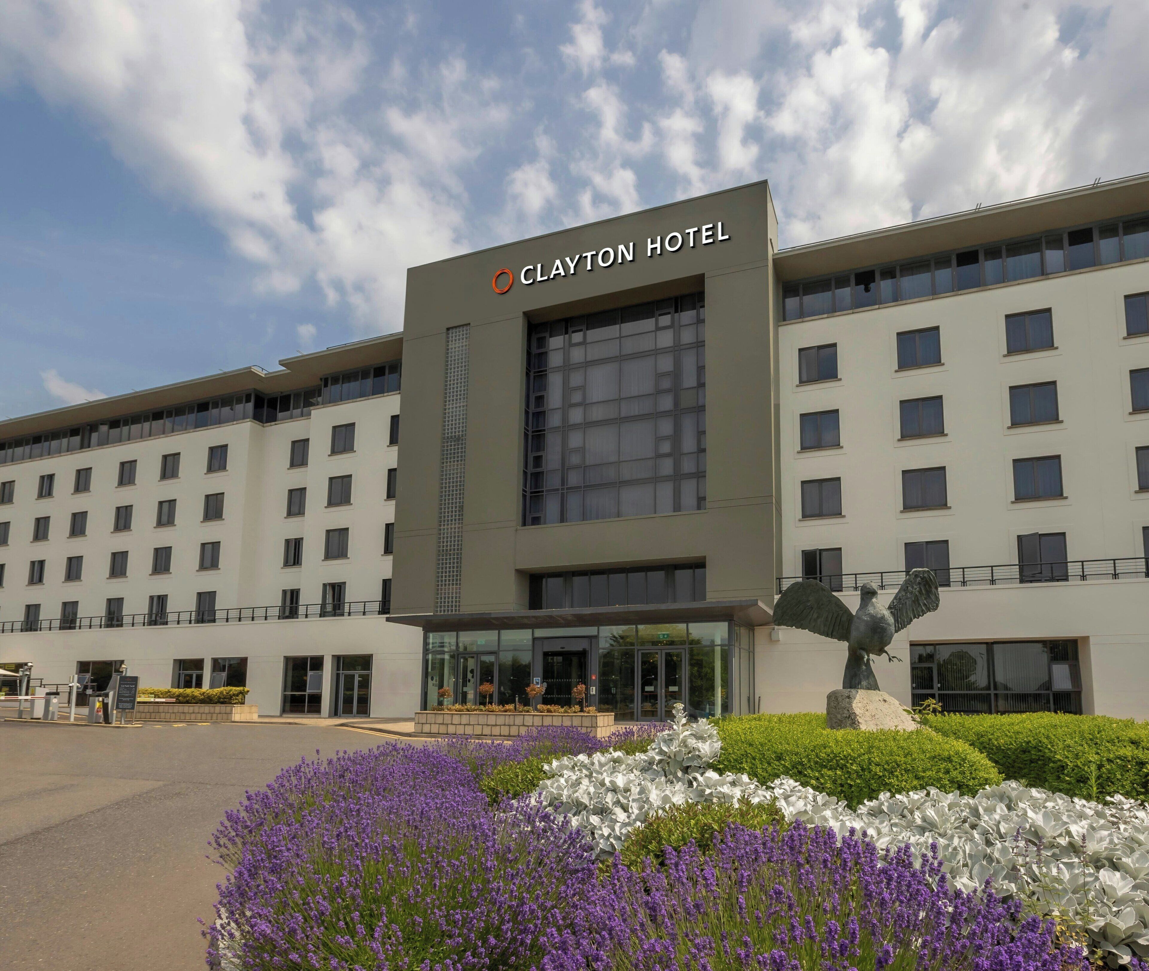 A Clayton Hotel building with a modern facade, large windows, and a statue of an eagle.