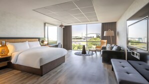 Una habitación de hotel moderna con una cama grande, un sofá, una mesita y vistas a la ciudad.